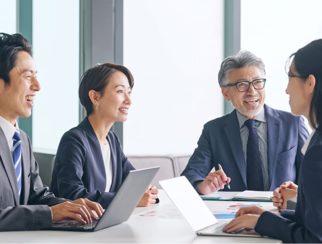 ノートパソコンを使いながらテーブルで和やかにミーティングをしている写真