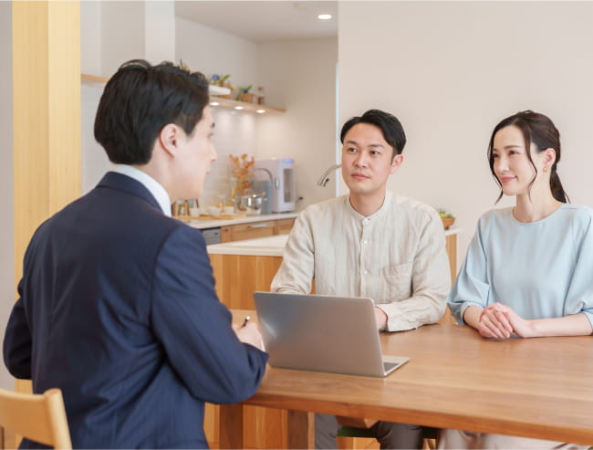 ビジネスマンがテーブルに座る男女にノートパソコンを見せながらコンサルティングをしている写真